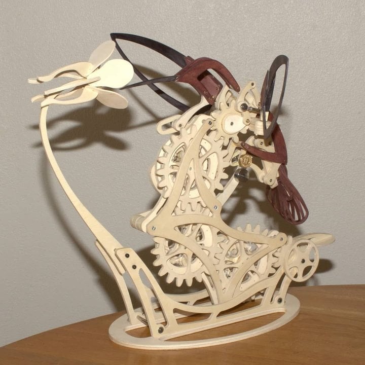 Mechanical model of a horse with gears on a wooden base against a Puzzloria | Kinetic Hummingbird Sculpture - 3D Wooden Mechanical Puzzle Kit