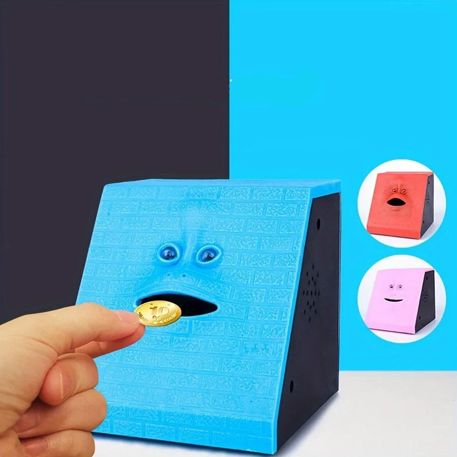 Blue money box with face design on a white surface, with a hand inserting a coin.