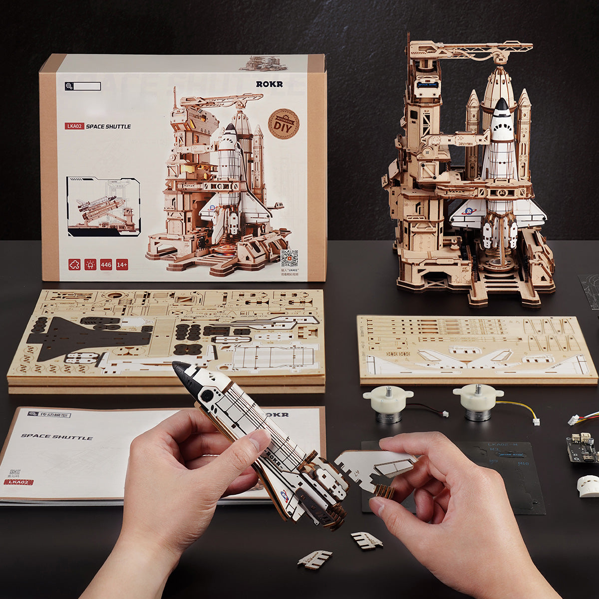 Wooden space shuttle model kit with packaging and assembly instructions on a dark surface.