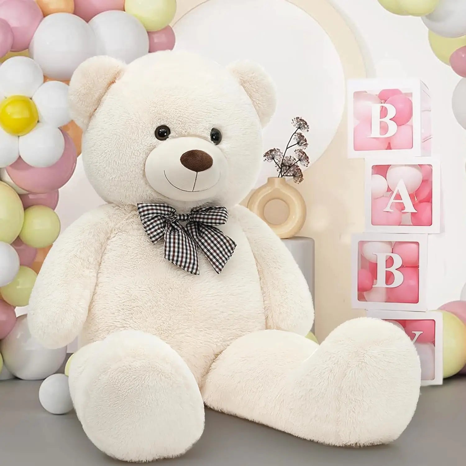 White teddy bear with a black bow tie in front of balloons and 'BABY' blocks.