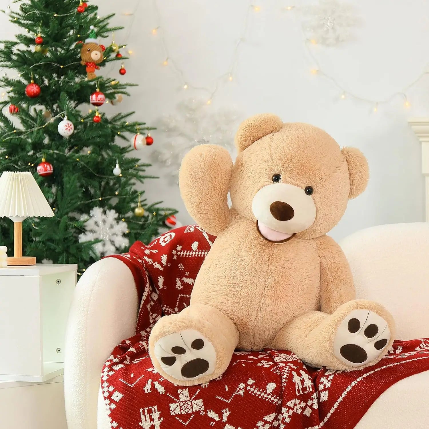Large teddy bear sitting on a red blanket with a Christmas tree in the background