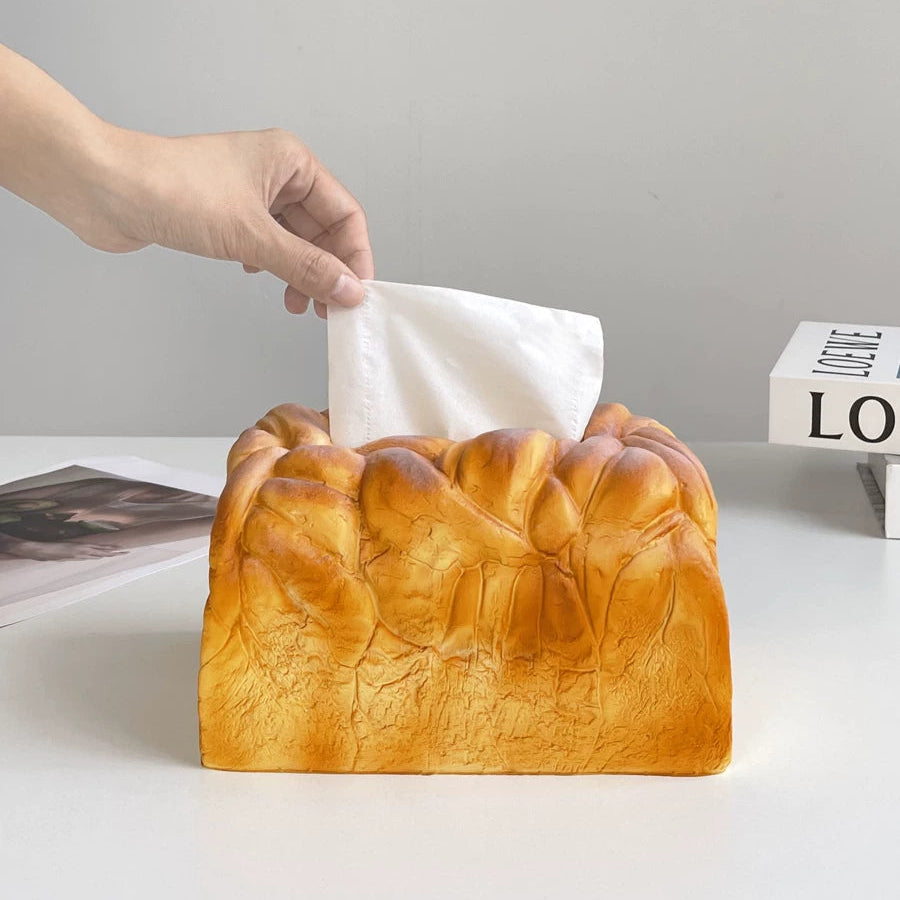 Bread-shaped tissue box with a hand pulling out a tissue against a neutral background