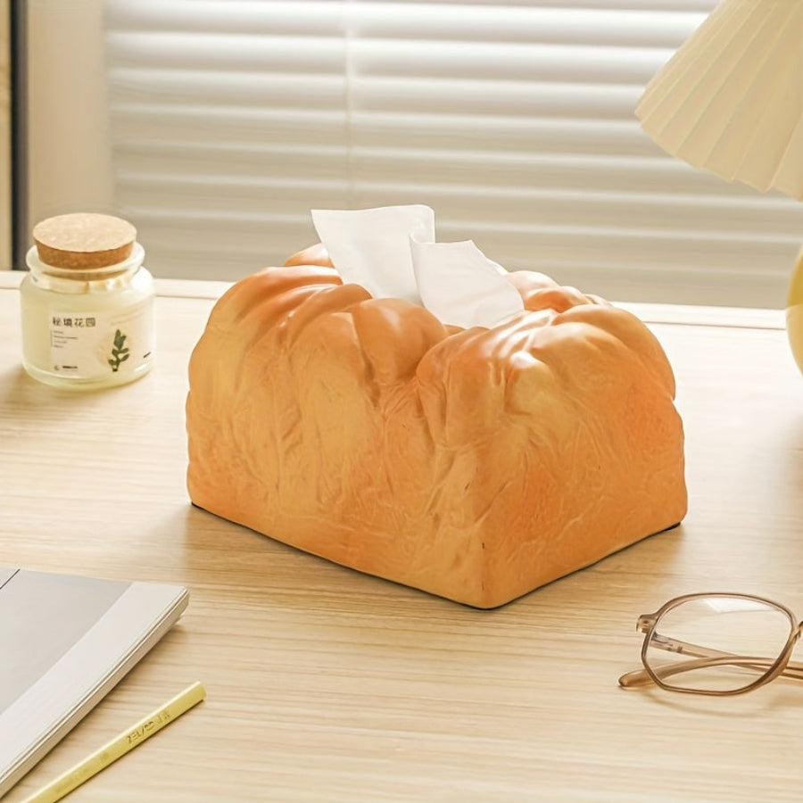 Bread-shaped tissue box on a desk with a lamp and glasses in the background