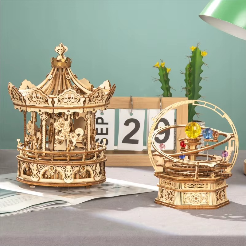 Two wooden mechanical models on a table with a calendar and cactus in the background.