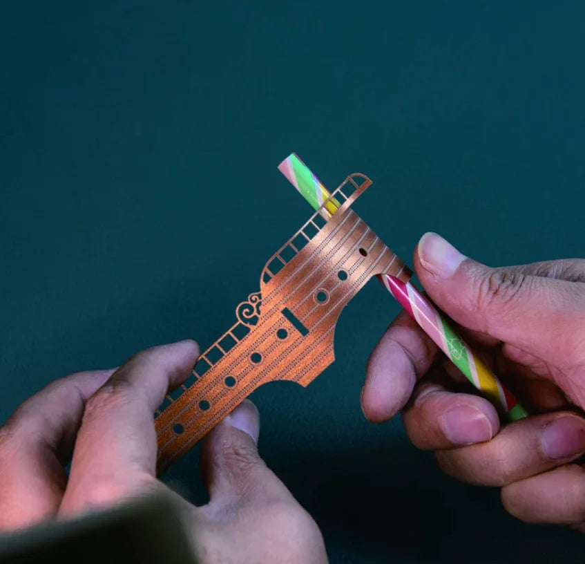 hands fitting an iridescent sail into the carved airship hull, hands on wooden model building hobby for teens