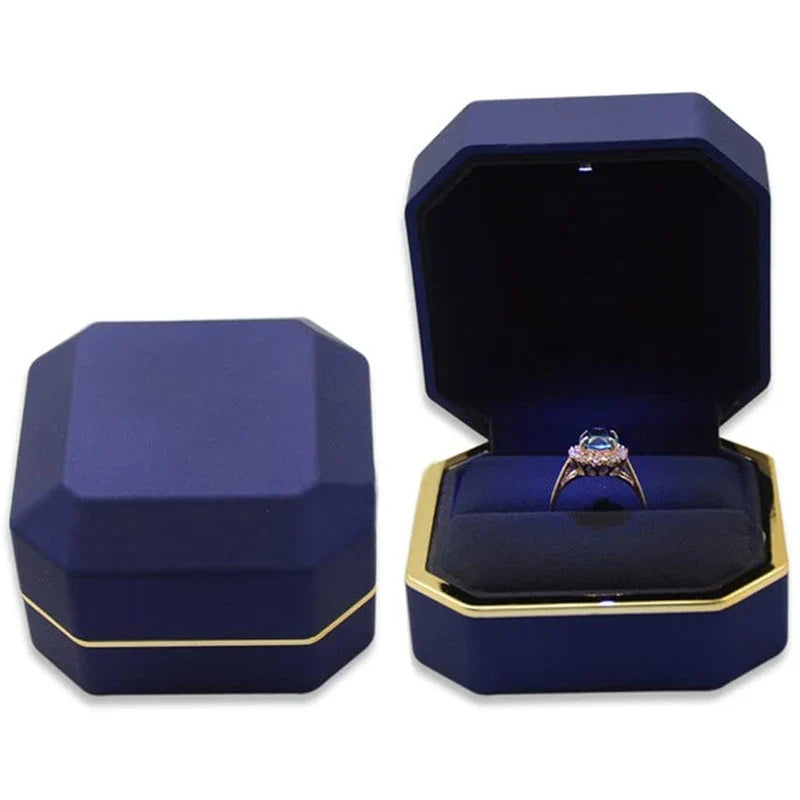 Navy octagon engagement ring box with gold trim and its LED light shining on a ring inside