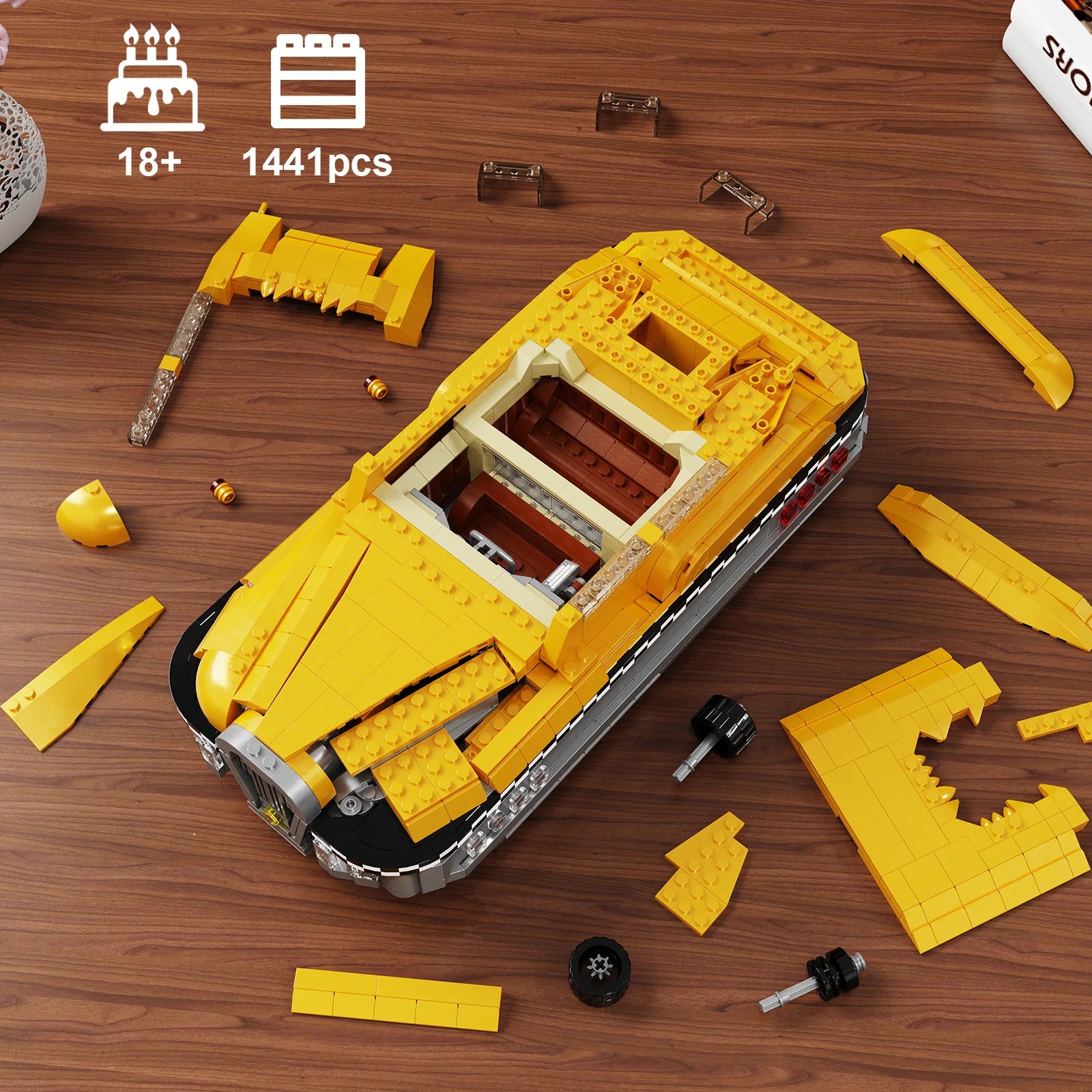 Yellow toy car model made from interlocking bricks on a wooden surface with building pieces scattered around.