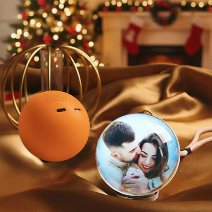 Orange spherical speaker on a gold surface with a decorative item featuring a couple, Christmas tree, and fireplace in the background.