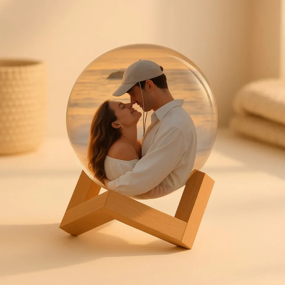 Glass orb with a wooden stand showing a reflection of a couple embracing, set against a beach backdrop.