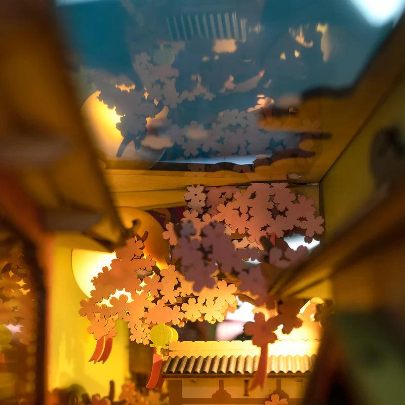 sakura blossom canopy detail glowing under warm led light in a japanese spring themed miniature bookshelf diorama
