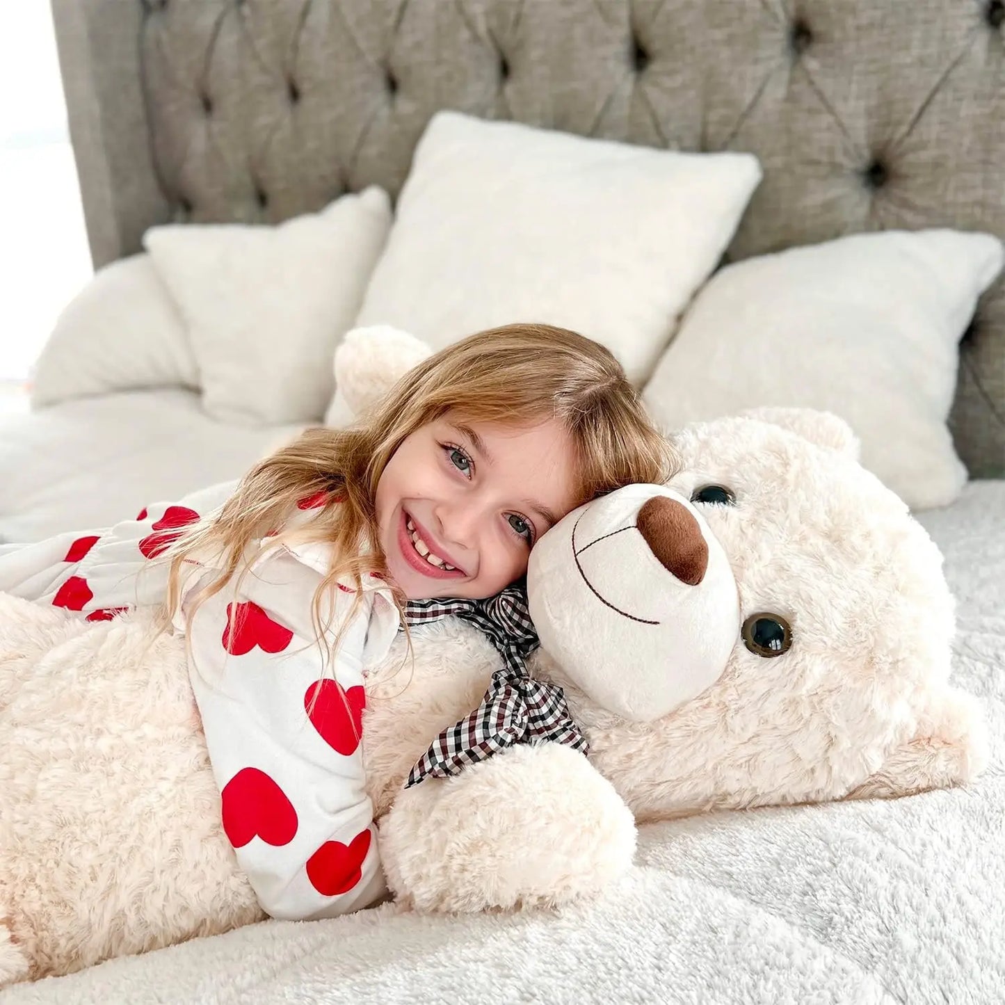 Child lying on a bed with a teddy bear and heart-patterned pillow