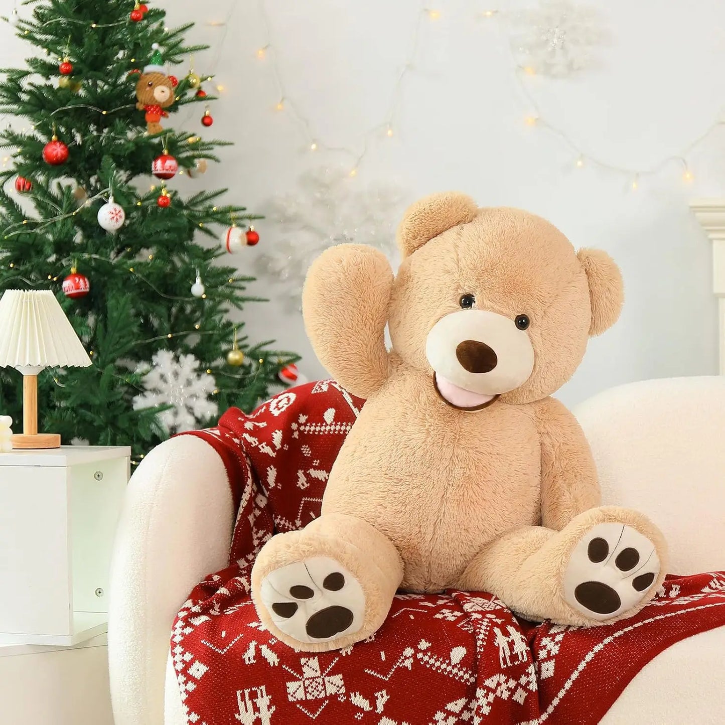 Large teddy bear sitting on a red blanket with a Christmas tree in the background