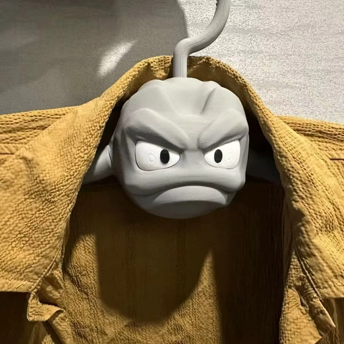 Pokemon Geodude hanger holding a yellow mustard jacket from its muscled rock monster arms, anti-slip clothes hanger